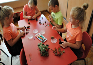 dzieci przy stoliku w sali robią ludziki z materiału przyrodniczego